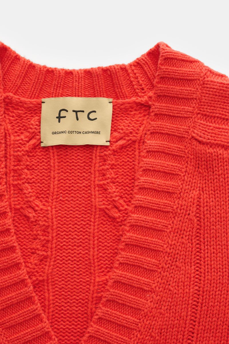 Nahaufnahme des FTC Cardigan hellrot von oben, zeigt V-Ausschnitt, Zopfstrick-Design, breite Rippbündchen, Bio-Baumwolle und Fair-Trade-Cashmere.