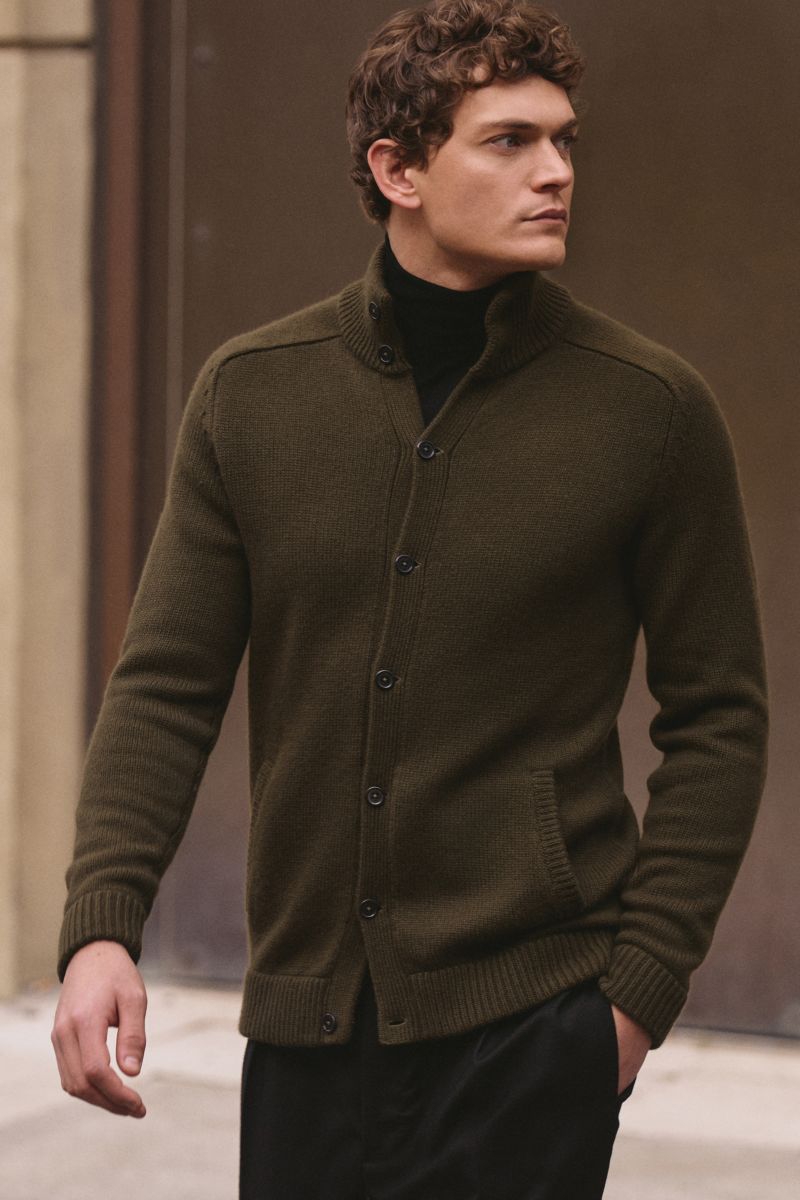 Junger Mann von vorne seitlich fotografiert trägt von Braun Cashmere Cardigan oliv aus reinem mongolischem Cashmere mit Stehkragen, Knopfleiste, Leistentaschen, Slim Fit und Rippbündchen.