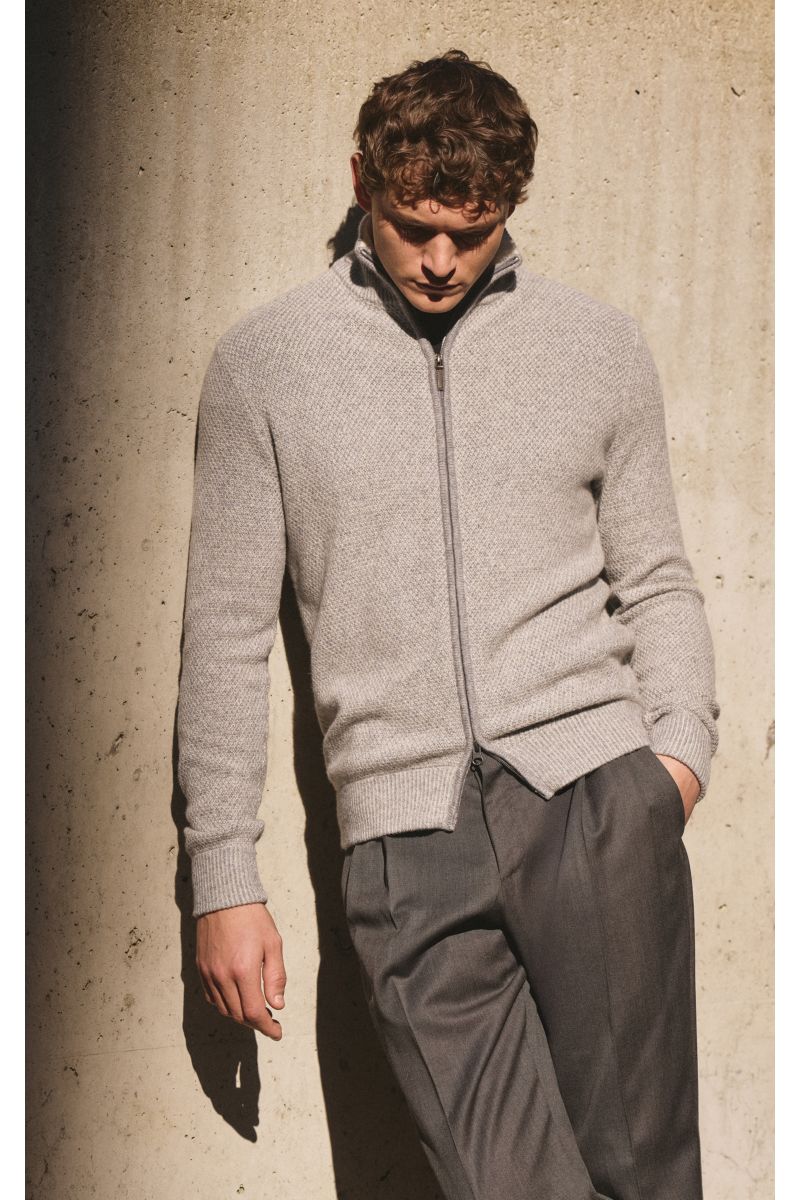 Mann lehnt vor Wand, trägt von Braun Cashmere Strickjacke grau meliert aus mongolischem Cashmere mit Strukturstrick, Slim Fit, Reißverschluss.
