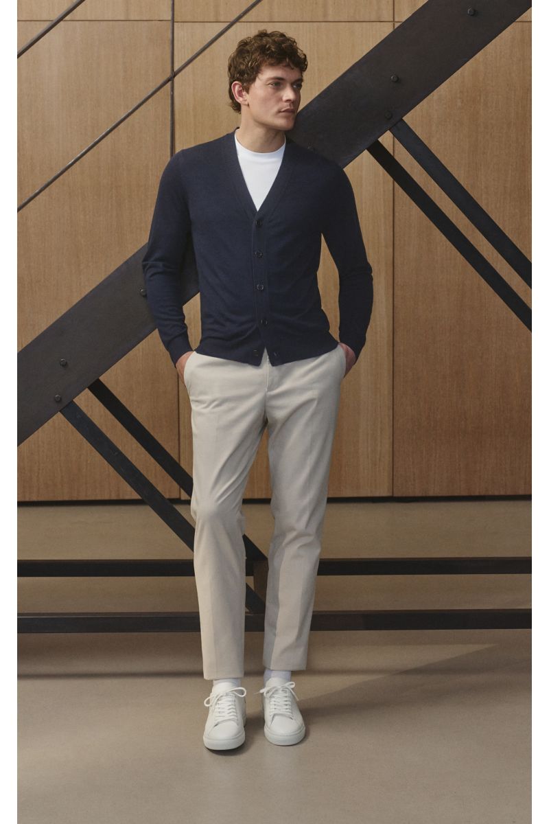 Mann stehend, seitliche Frontansicht, trägt von Braun Merino Cardigan navy aus reiner Merinowolle mit Perlmuttknöpfen, Regular Fit, feines Strickbild, elastische Bündchen.