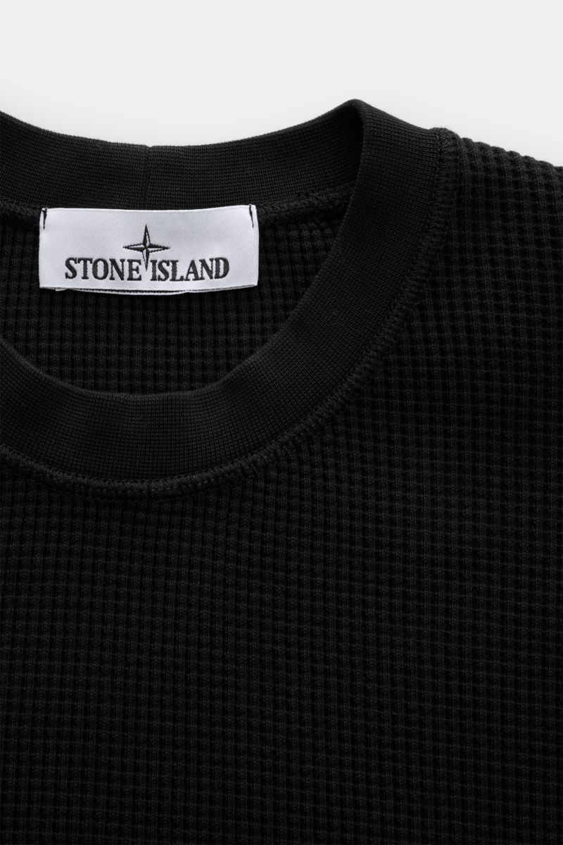 Close-up front view of Stone Island Rundhalspullover 'Waffle' schwarz in black waffle knit cotton with ribbed round neckline and brand label. Basic Piece mit Twist: Dieser Pullover im Waffelstrick von STONE ISLAND wird zur idealen Grundlage moderner Freiz