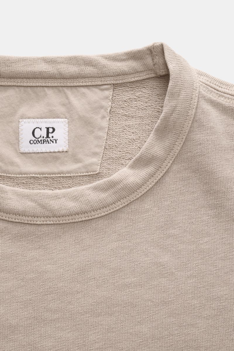 C.P. Company Rundhals-Sweatshirt beige shown from a close-up front perspective focusing on the collar, label, and textured cotton fabric. 