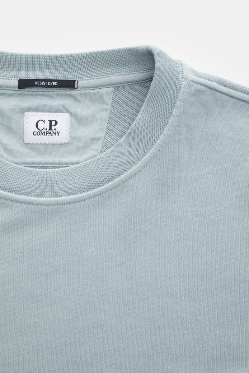 Close-up top-down view of the C.P. Company Sweatshirt smoky blue crew neck, showing pure cotton fabric, ribbed collar, and brand labels.