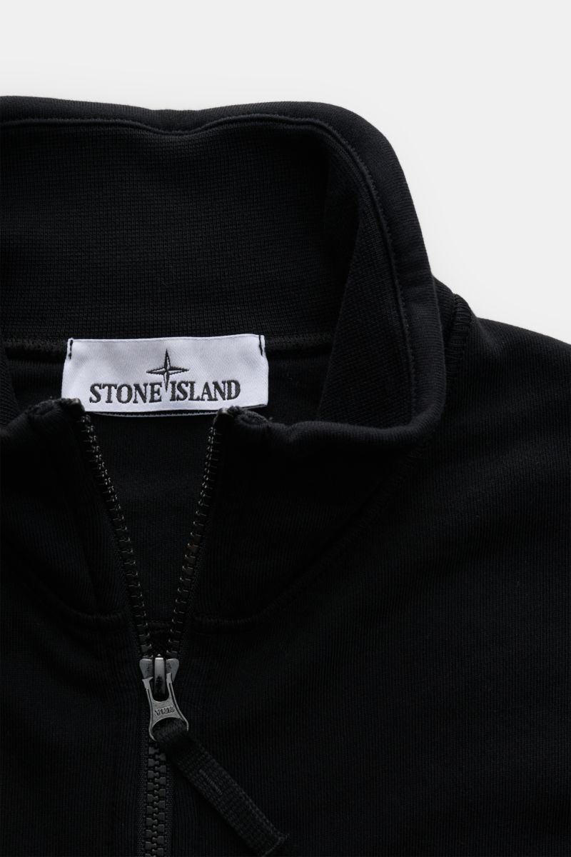 Close-up front view of the Stone Island Sweatjacke schwarz, showing the high collar, robust zipper, and brand label inside the collar. Entspanntes Basic von STONE ISLAND: Mit sportiver Lässigkeit begleitet uns die stückgefärbte Sweatjacke aus softer Ba