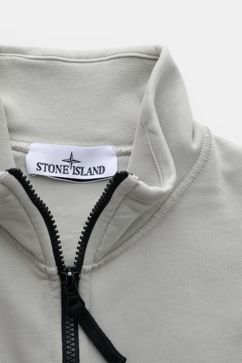 Nahaufnahme der Stone Island Sweatjacke hellgrau von vorne oben, zeigt hochschließenden Stehkragen, robusten Reißverschluss und weiche Baumwolle.