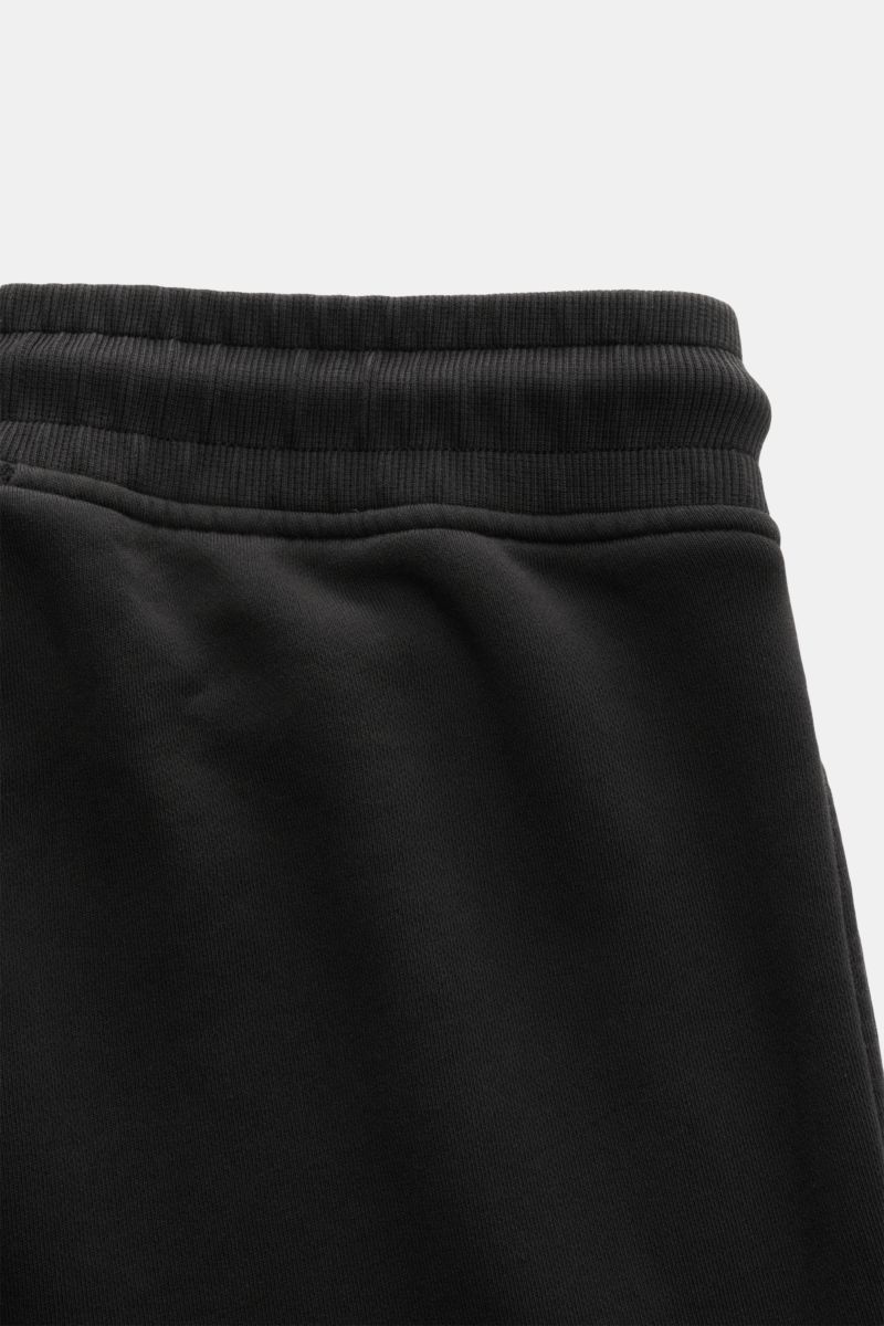 Close-up front view of the waistband and upper section of the C.P. Company Cargo-Sweathose schwarz, made from soft, pure cotton sweat fabric with a slim fit, short cut, elastic waistband with drawstring, side seam pockets, cargo pocket with lens detail, a