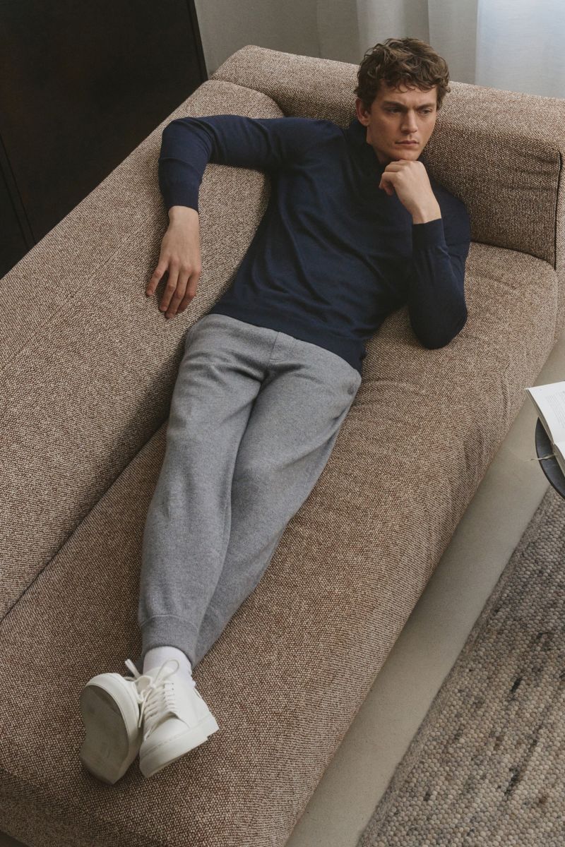 Mann liegt seitlich auf braunem Sofa, trägt von Braun Cashmere Jogpants navy, grau, tapered fit, hoher Bund, elastischer Tunnelzug.