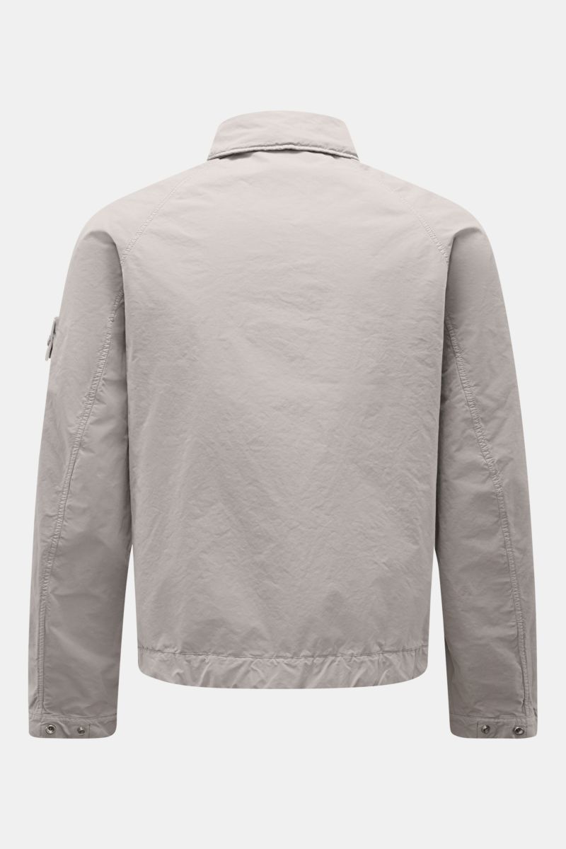 Stone Island Jacket 'Ghost Piece' light grey shown from the back, featuring high-quality microfibre, soft feel, slim fit, snap button placket, turn-down collar with buttoned tab, front flap pockets, tonal compass badge on upper sleeve, and snap button cuf