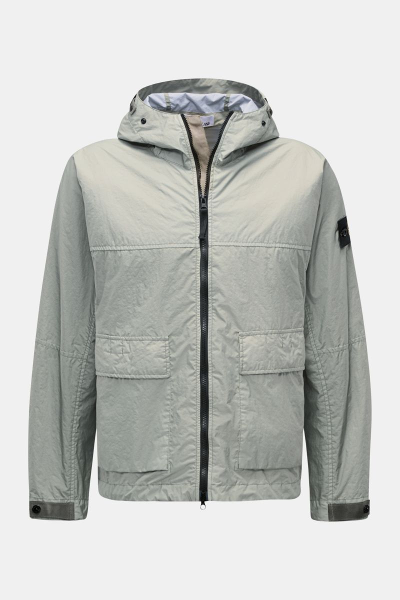 Front view of Stone Island Jacket 'Membrana' sage in light green, featuring a drawstring hood, two patch front pockets, cuffs with buttons, and a black compass badge on the upper sleeve. Function meets style: made from high-quality microfibre with a light