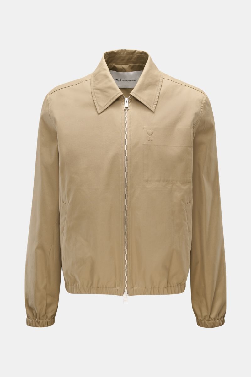 Front view of Ami Paris Blouson taupe, a slim fit jacket in pure cotton with soft touch, featuring a two-way zipper, turn-down collar, logo stitching on chest pocket, slanted welt pockets, elastic hem and cuffs, and an inner pocket. Stylish companion for 