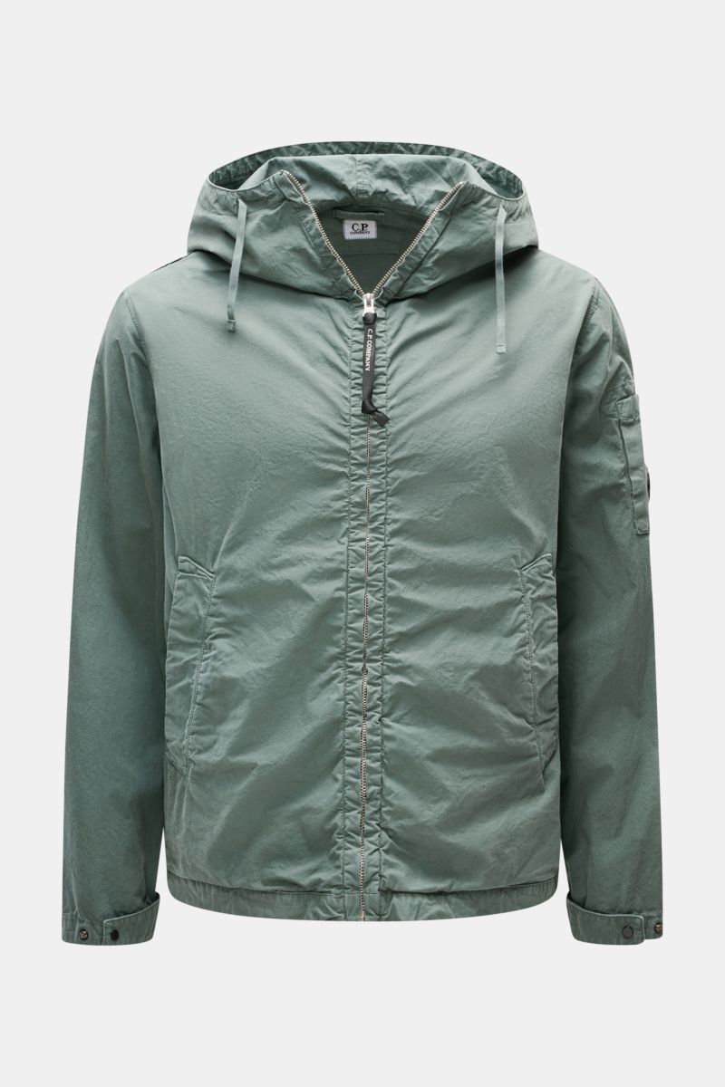 Front view of a C.P. Company Jacket sage in light green, hooded with drawstrings, metal zip, slanted hip pockets, adjustable cuffs and hem, made of lightweight, garment-dyed pure cotton Micro-Reps fabric with a soft feel, featuring a logo detail on the sl