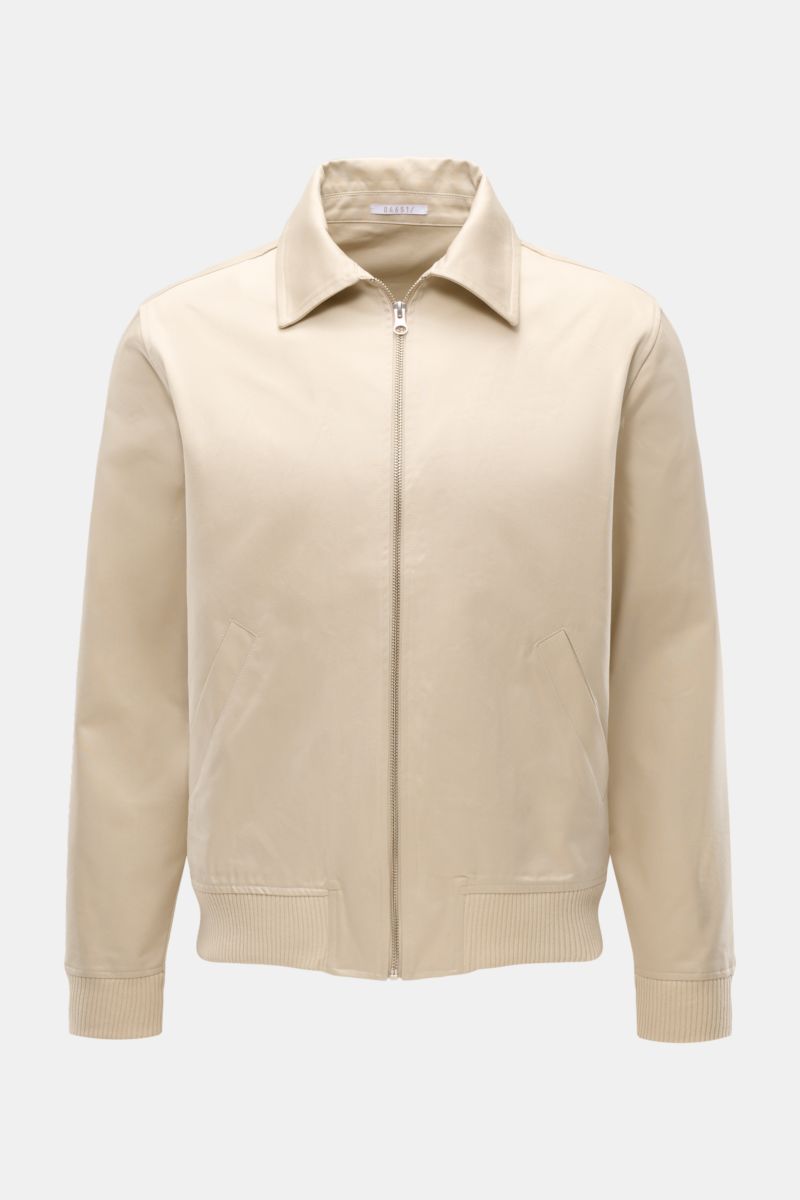 Front view of 04651/ A trip in a bag Blouson 'Griffin' beige, a slim fit cotton jacket with soft touch, zip closure, collar, elastic cuffs and hem, piped pockets, unconstructed design, and inner pocket, showcasing casual retro style.