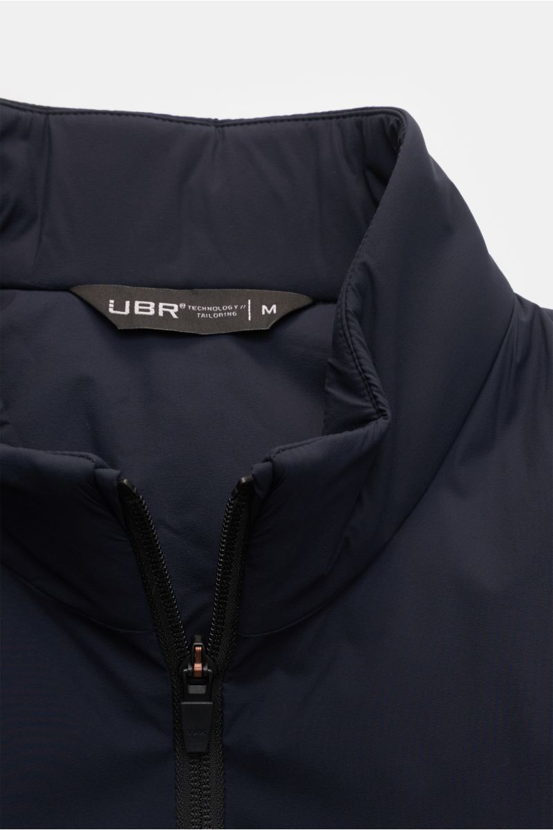 Close-up front view of UBR Outdoor-Weste 'Raptor' navy with high collar, two-way zipper, and soft microfiber fabric, showing label inside. Leichtigkeit, die man spürt – Performance, die bleibt: Mit der Weste 'Raptor' zeigt UBR, wie moderne Essentials auss