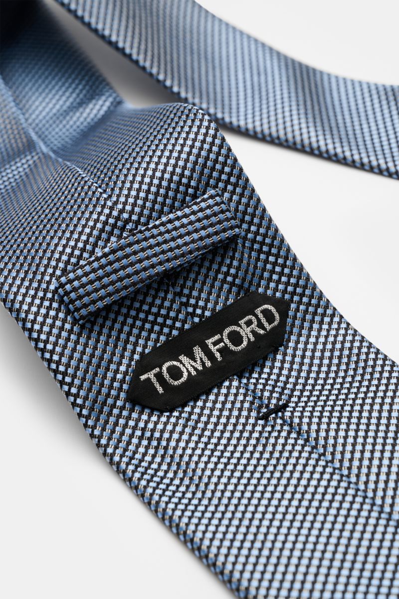 Close-up angled view of the Tom Ford Seidenkrawatte hellblau/schwarz/grau gemustert showing its fine graphic weave and branded label. 

Italienische Handwerkskunst: Dieser Krawatten-Klassiker von TOM FORD aus reiner Seide vereint zeitlose Eleganz mit e