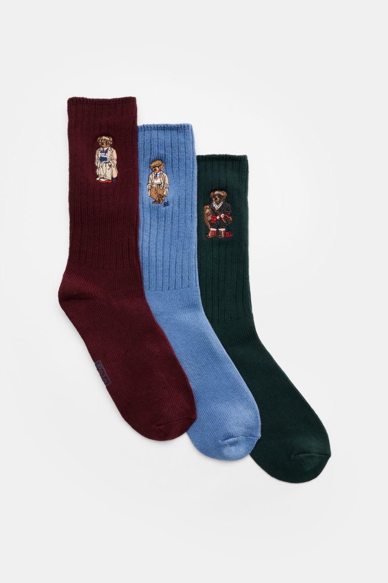 Front view of Polo Ralph Lauren Strümpfe 3er-Set grün/navy/rot with three ribbed socks in burgundy, blue, and dark green, each featuring a distinctive Teddy bear print. Stylishe Statements für die kalte Jahreszeit: Die Strümpfe mit dem charakteristisch