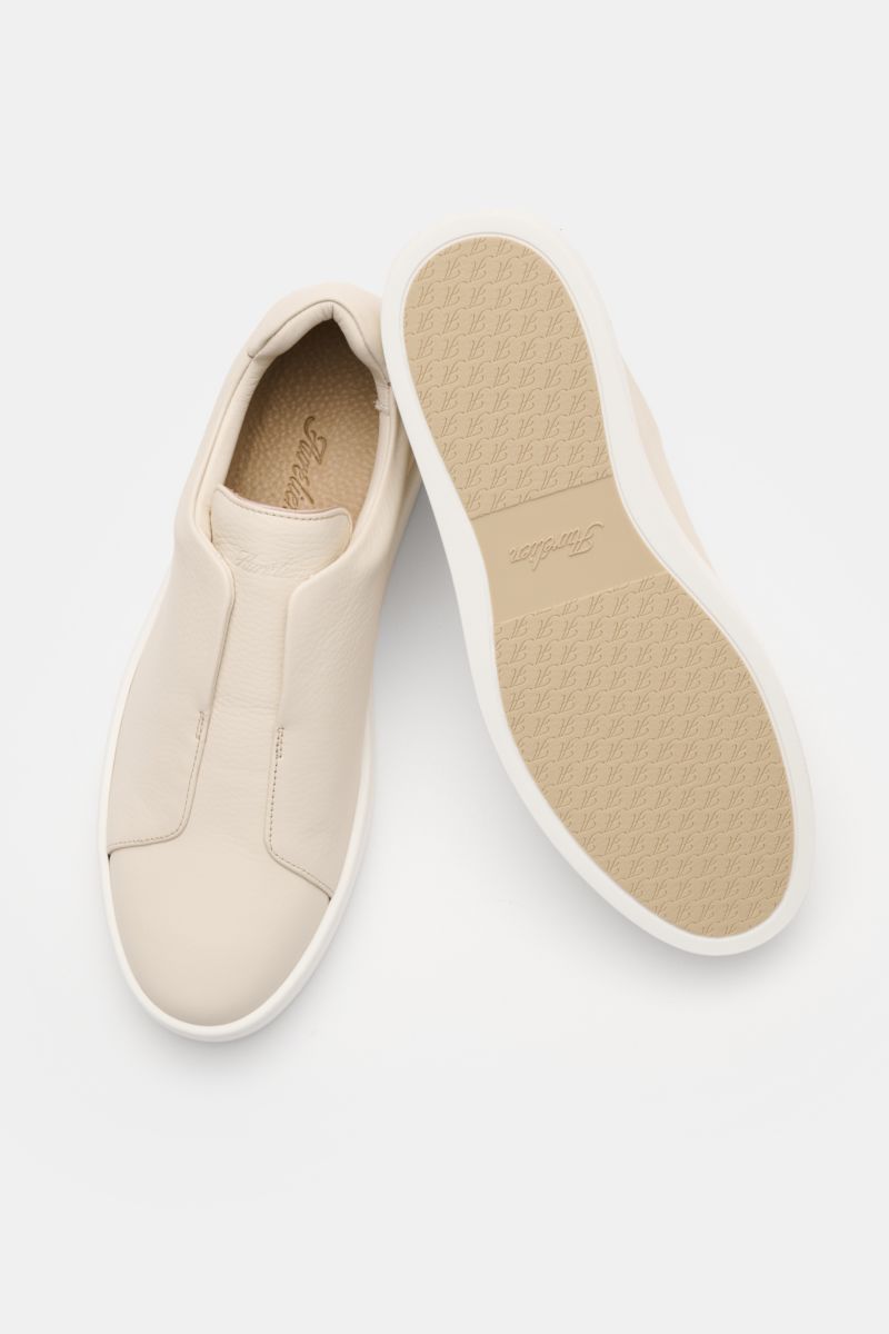 Aurélien Slip-on-Sneaker creme shown from top and sole view, minimalist design with finely grained leather, round toe, elastic bands inside, padded collar, subtle logo embossing, leather lining, flexible rubber sole for comfort and elegance.