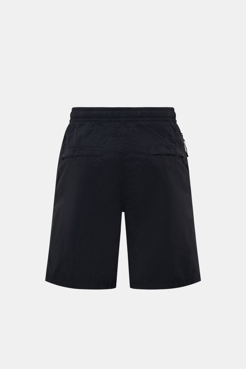 Stone Island Swim shorts 'Ghost Piece' dark navy shown from the back, featuring elastic waistband, zippered side & back pockets, French pockets, mesh lining, high-quality microfibre, robust feel, regular fit, and monochrome woven label at hem. A monochrom