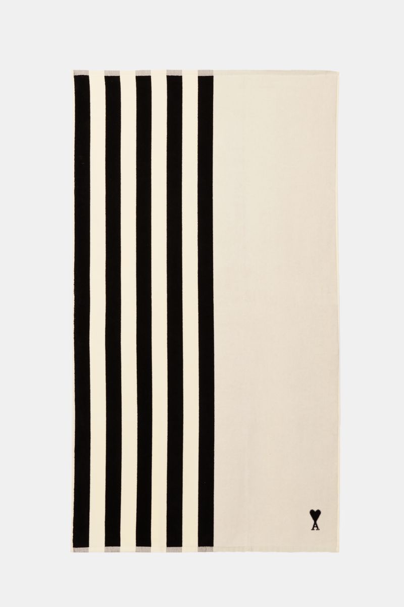 Ami Paris Strandtuch schwarz/weiß gestreift shown from above, featuring vertical black and white stripes on one side and solid white on the other with a small black logo. Luxuriöser Begleiter für sonnige Tage: Mit seinem ikonischen Streifendesign und d
