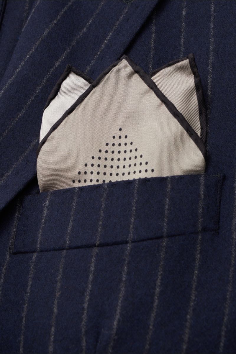 Close-up front view of Tom Ford Pocket square grey/black dotted tucked into a navy pinstripe jacket pocket, featuring pure silk, smooth touch, modern dotted design, hand-rolled edges, small TOM FORD logo, made in Italy, dimensions 40 cm x 40 cm.