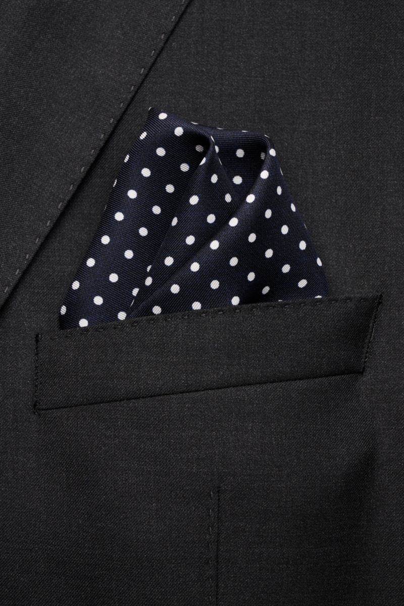 Rosi Collection Seiden-Einstecktuch navy gepunktet, aus reine Seide, geschmeidig mit grafischem Punktmuster, handrollierte Kanten, Made in Italy, ca. 31x31 cm, frontale Nahaufnahme in Brusttasche eines schwarzen Sakkos.