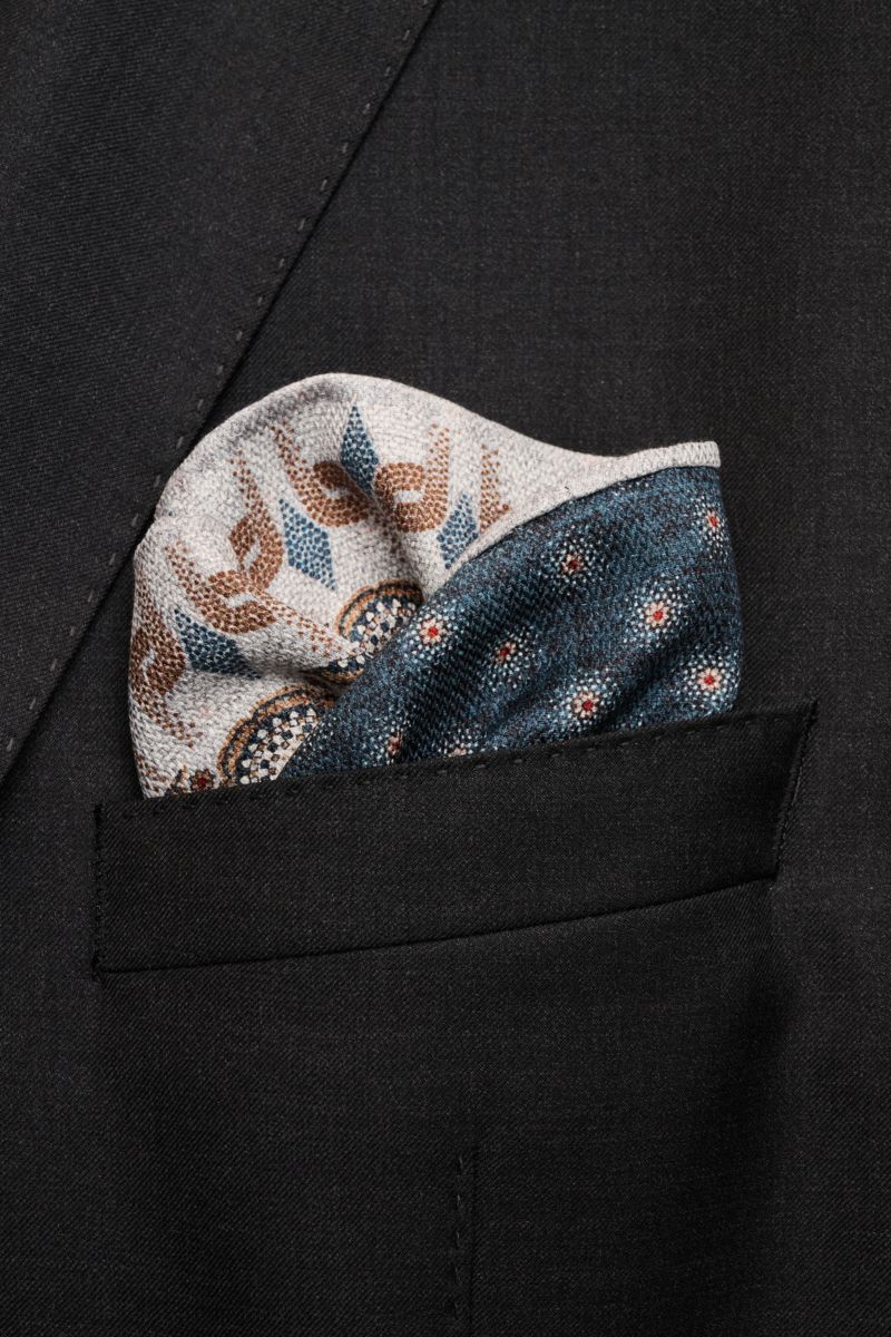 Rosi Collection Seiden-Einstecktuch 'Easy' grau/braun/graublau gemustert, reine Seide, softer Griff, Kachel-Muster, gepunktete Rückseite, rollierte Kanten, Made in Italy, ca. 31x31 cm, steckend in schwarzer Sakko-Tasche, frontale Nahaufnahme.