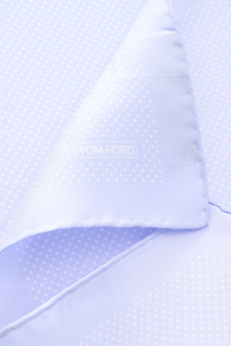 Close-up image of the Tom Ford Seiden-Einstecktuch hellblau/weiß gepunktet, showing the folded corner with rollierte Kanten and subtle TOM FORD print, photographed from a top-down perspective. Dieses Einstecktuch von TOM FORD aus reiner Seide setzt mit se