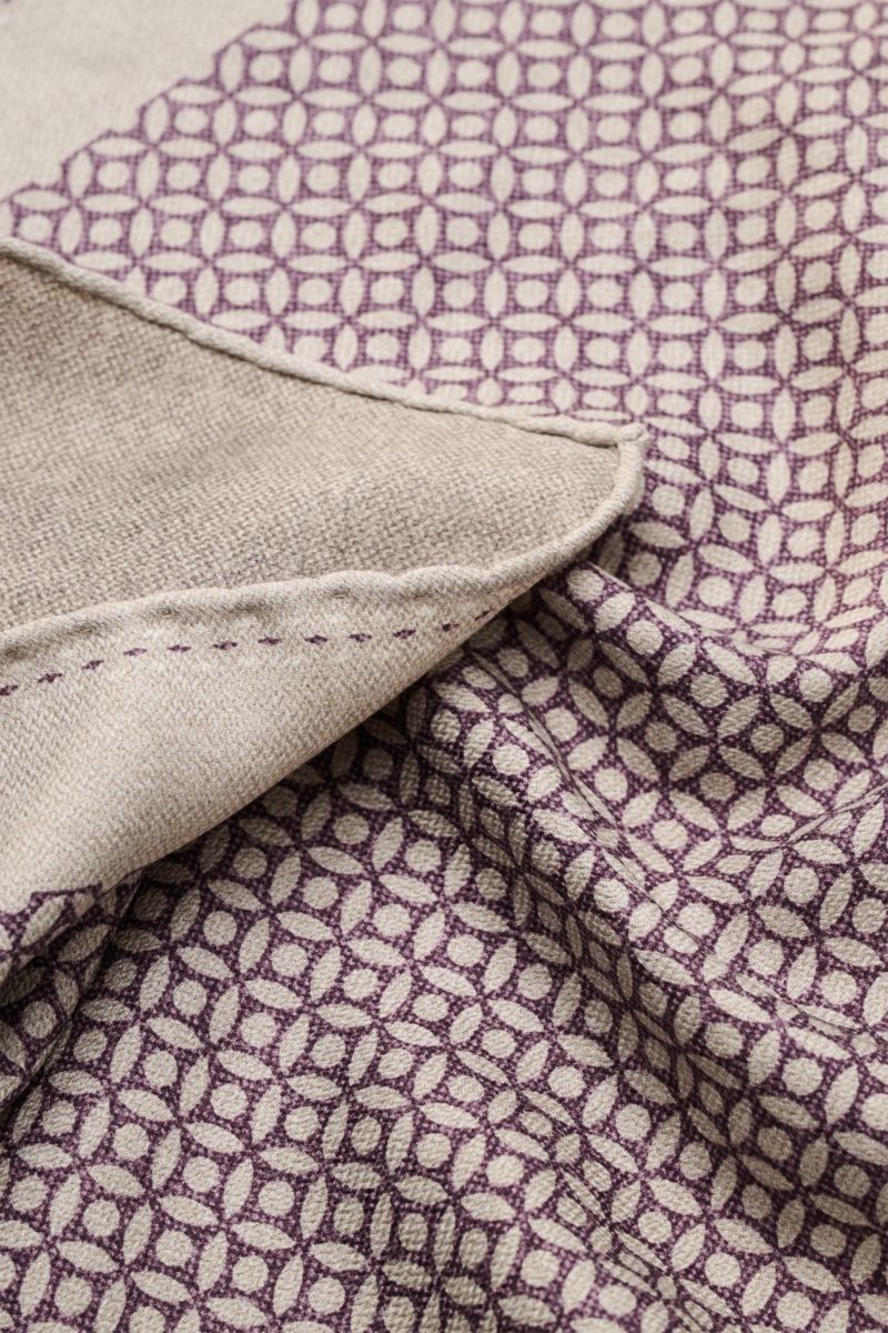 Nahaufnahme des Brunello Cucinelli Seiden-Einstecktuchs sand/violett gemustert mit floralem Muster, handrollierten Kanten, reiner Seide, geschmeidigem Griff, Maße ca. 35 x 35 cm, Made in Italy, aus schräger Perspektive fotografiert.