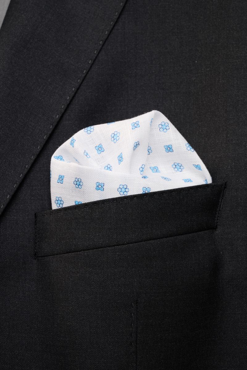 Rosi Collection Linen pocket square 'Fox' white/light blue patterned, soft pure linen with floral print and rolled edges, made in Italy, 31.5x31.5 cm, shown folded in a black jacket pocket from a close-up front angle.