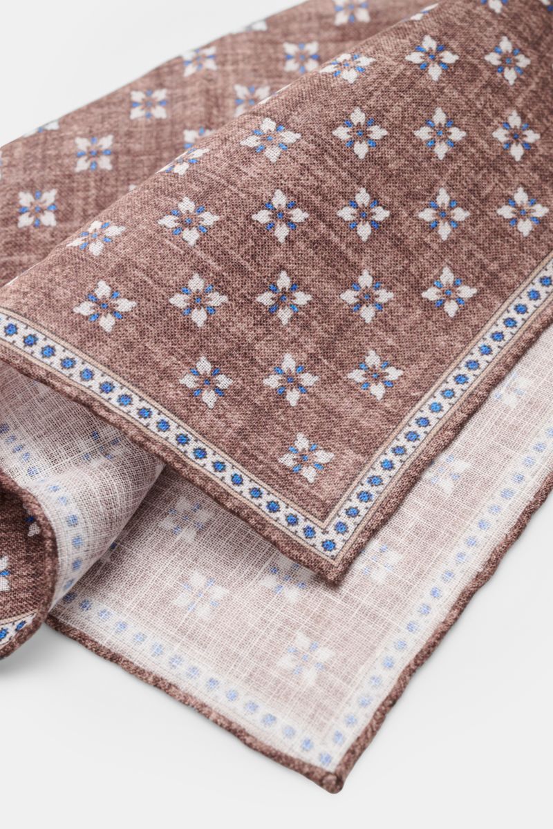 Rosi Collection Linen pocket square 'Fox' brown/blue/off-white patterned, folded and shot from a close-up angle showing floral print with edging, rolled edges, pure linen, soft feel, made in Italy, dimensions 31 cm x 31 cm.