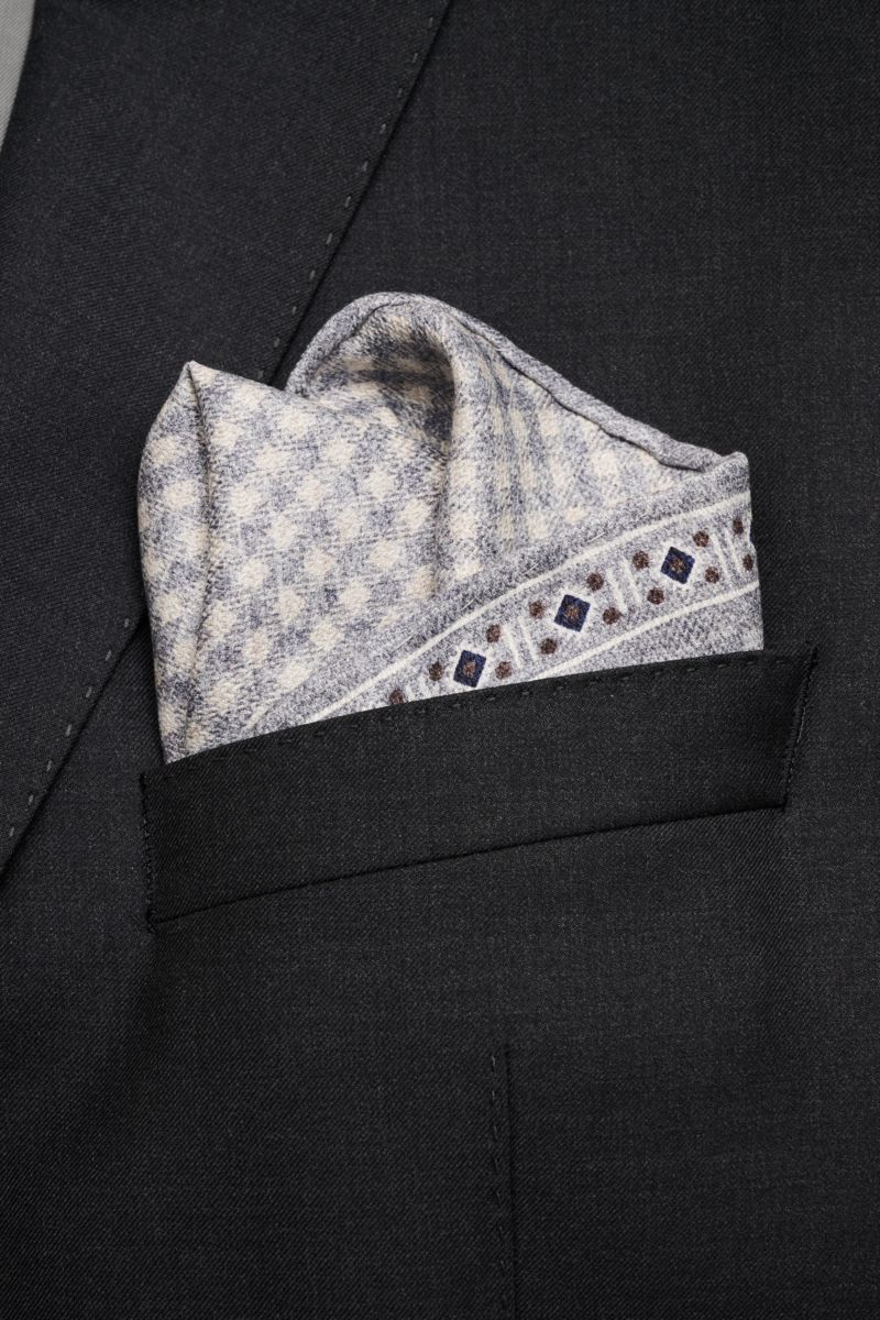 Brunello Cucinelli Seiden-Einstecktuch grau/weiß/navy gemustert folded in a black suit pocket, photographed close-up from the front.  
Zeitloser Akzent für besondere Momente: Das Einstecktuch aus reiner Seide von BRUNELLO CUCINELLI verleiht jedem Look 