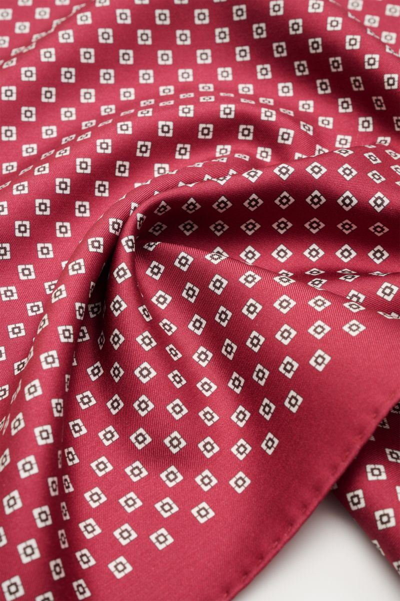 Close-up, angled top view of the Brunello Cucinelli Seiden-Einstecktuch dunkelrot/hellgrau/navy gestreift showing its smooth silk fabric with a subtle striped pattern and hand-rolled edges.

Description: Quiet Luxury heißt der große Trend: Das kann BRU