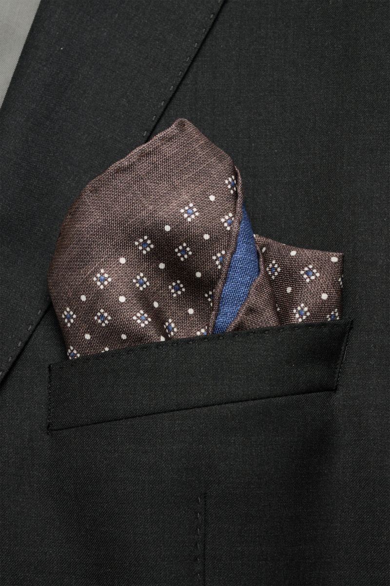Close-up front view of a Brunello Cucinelli Seiden-Einstecktuch dunkelblau/graubraun/weiß gemustert pocket square in a black jacket pocket, featuring a graphic pattern.

Quiet Luxury kann BRUNELLO CUCINELLI besonders gut und bringt auch in dieser Saiso
