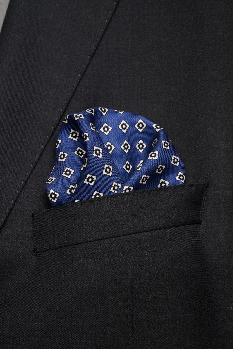 Close-up of a blue patterned Brunello Cucinelli Seiden-Einstecktuch taupe/schwarz/weiß gemustert in a dark suit pocket, photographed from above.

Quiet Luxury kann BRUNELLO CUCINELLI besonders gut und bringt auch in dieser Saison passende Einstecktüche