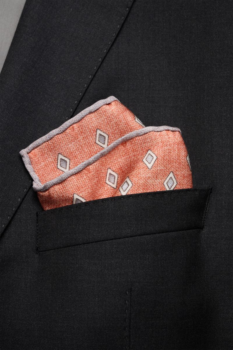 Brusttasche eines schwarzen Sakkos mit elegant gefaltetem Brunello Cucinelli Seiden-Einstecktuch rostbraun/grau/hellgrau gemustert, feines Rautenmuster, rollierte Kanten in Kontrastfarbe, reine Seide, glatter Griff, Maße ca. 35x35 cm, Made in Italy.