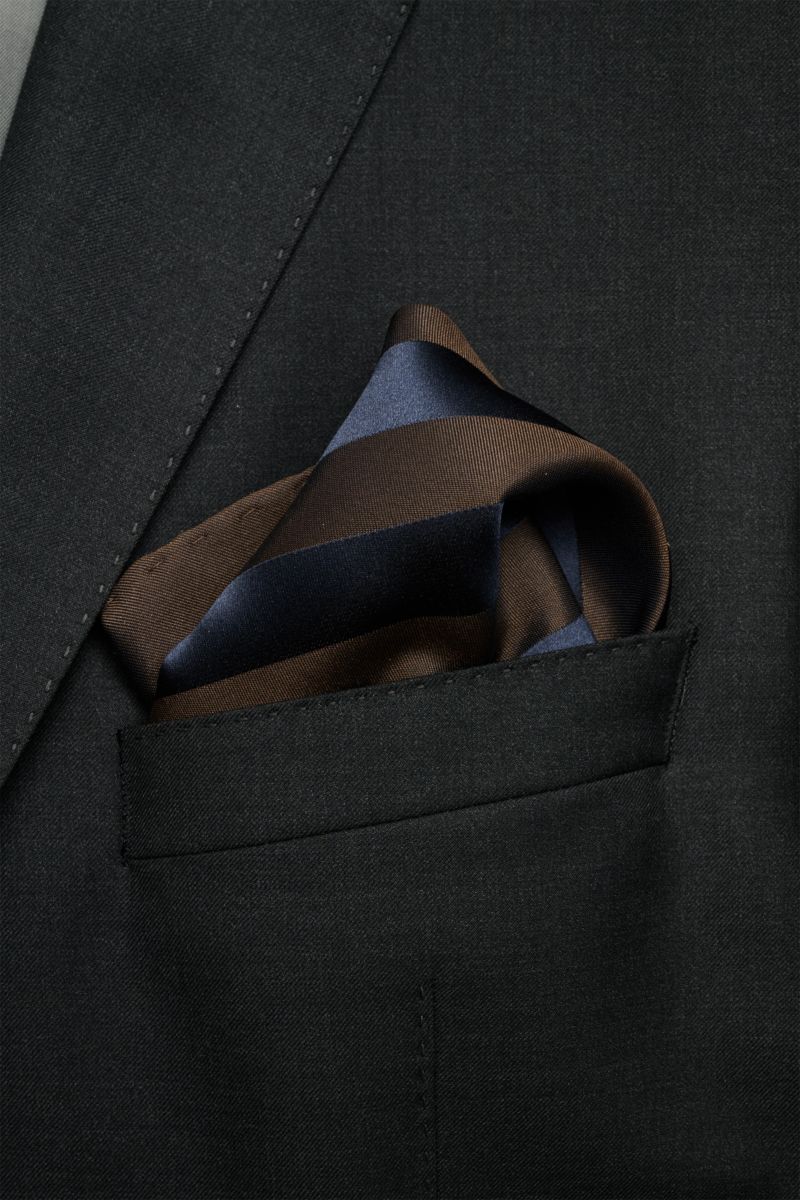 Brunello Cucinelli Seiden-Einstecktuch dunkelbraun/dark navy gestreift folded in a black suit pocket, photographed close-up from front top angle. Eleganter Akzent: Das Einstecktuch aus reiner Seide von BRUNELLO CUCINELLI überzeugt mit seinem edlen Stre