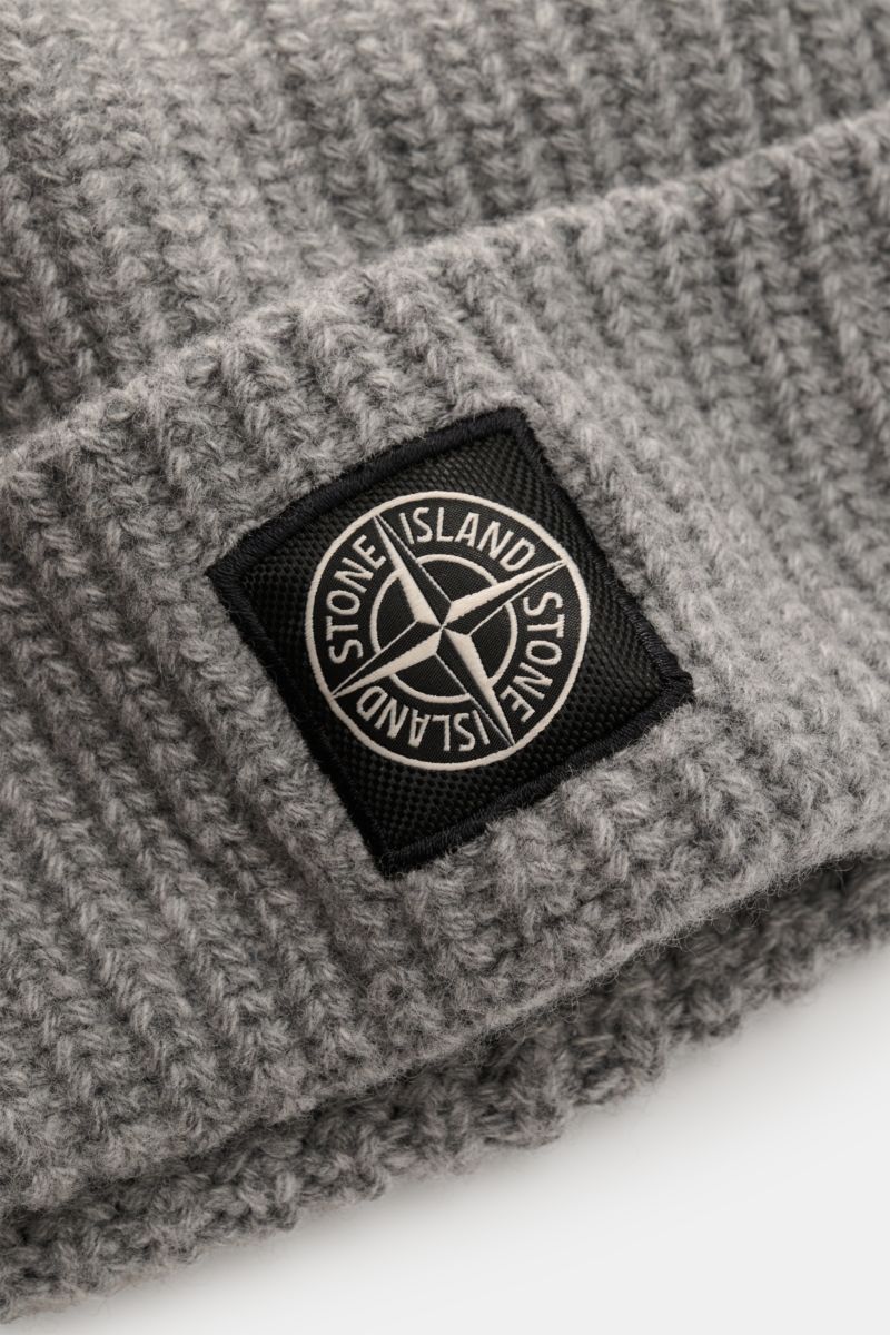 Stone Island Wollmütze grau meliert aus reiner Wolle, leicht griffig, moderne Rippstrick-Optik, breiter Umschlag, Front mit STONE ISLAND-Weblabel, Nahaufnahme schräg von oben.