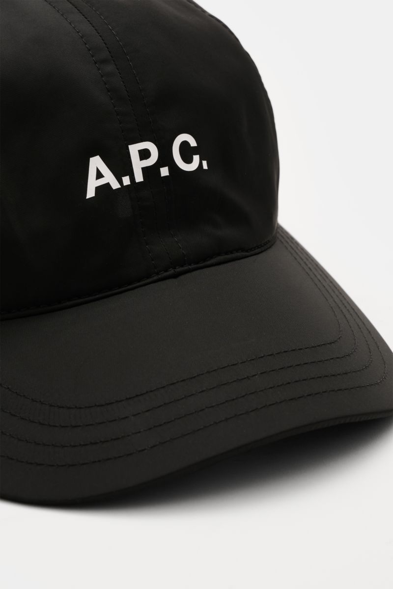 Close-up front-side view of the A.P.C. Baseball-Cap 'Charlie' schwarz in black lightweight microfiber, featuring a classic six-panel design, white logo print on front, and adjustable closure. Lässiger Urban Style aus Paris: Die Baseball-Cap 'Charlie' aus 
