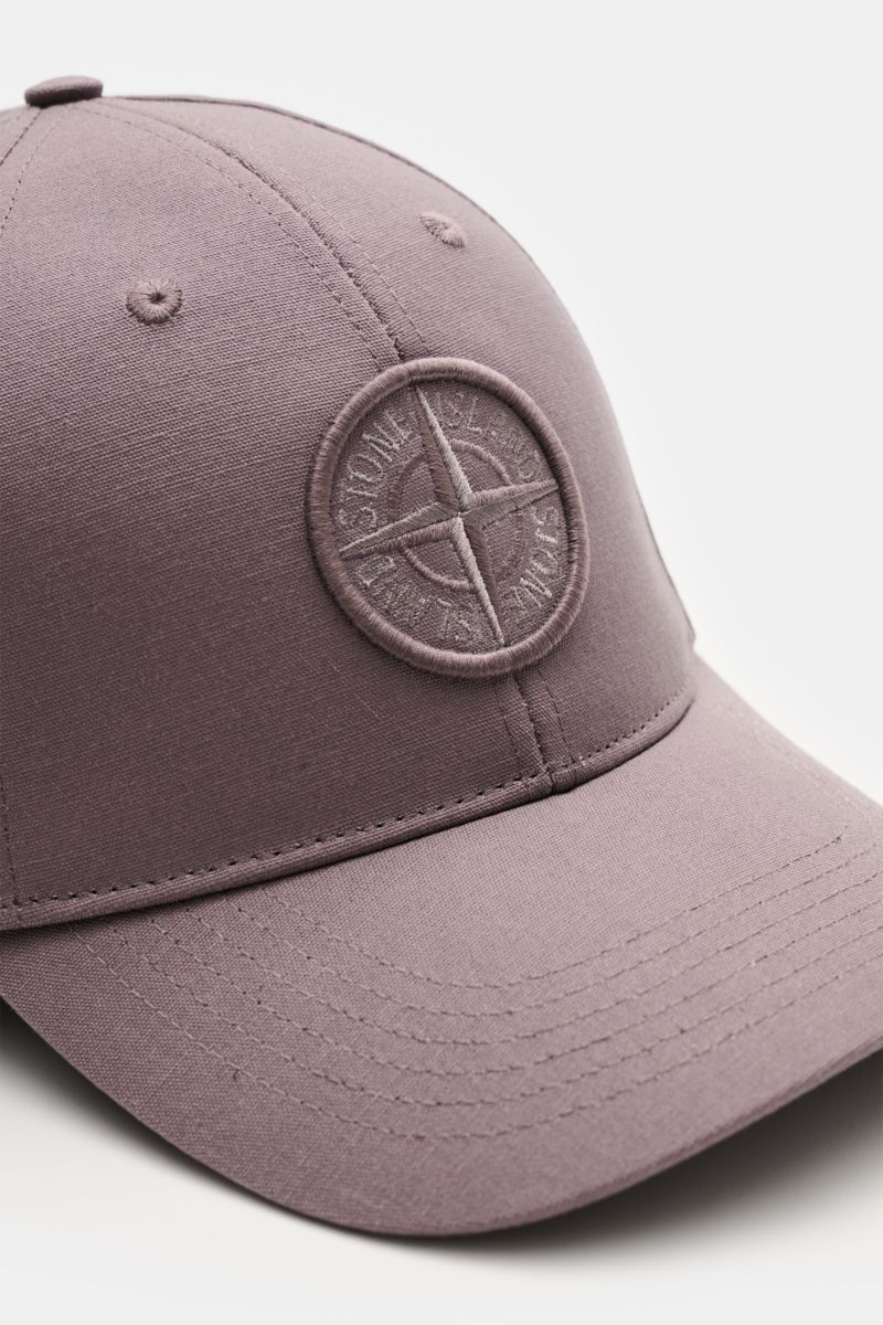 Stone Island Baseball-Cap violett shown from a front-side angle, made of pure cotton with a curved brim, tonal compass-stitching, and adjustable closure. Lässig mit Stil: Diese Baseball-Cap aus reiner Baumwolle von STONE ISLAND ergänzt Ihren Look mit tona