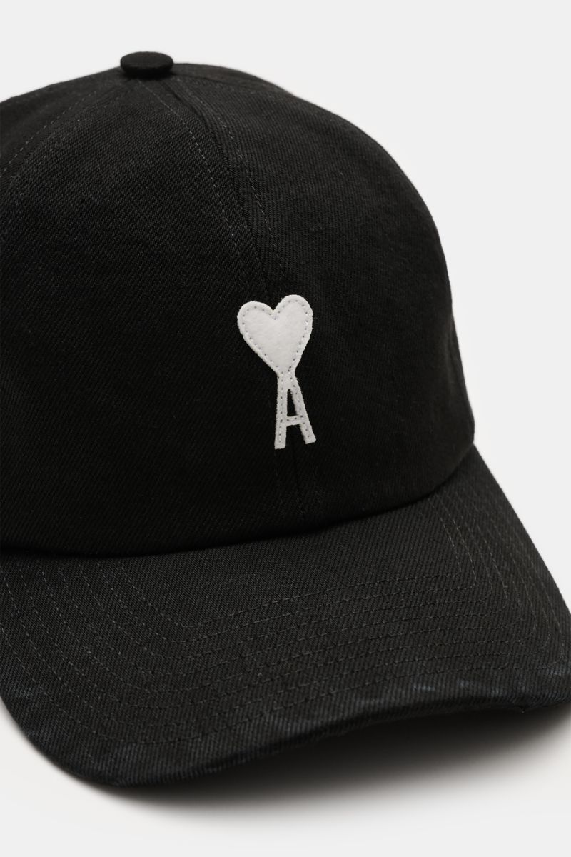 Ami Paris Baseball-Cap schwarz shown from a front angled perspective, made of pure cotton with a soft feel, curved brim, adjustable closure, and a white heart-shaped logo patch on the front. A french affair: Diese Baseball-Cap aus reiner Baumwolle von 