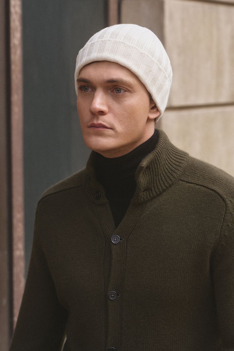 Porträtfoto eines Mannes von vorne mit fokus auf die von Braun Cashmere Mütze offwhite, fein gestrickt mit klassischem Rippmuster, schmalem Umschlag, aus reinem mongolischem Cashmere, sehr weich, passend zu Wintermantel oder Daunenjacke.