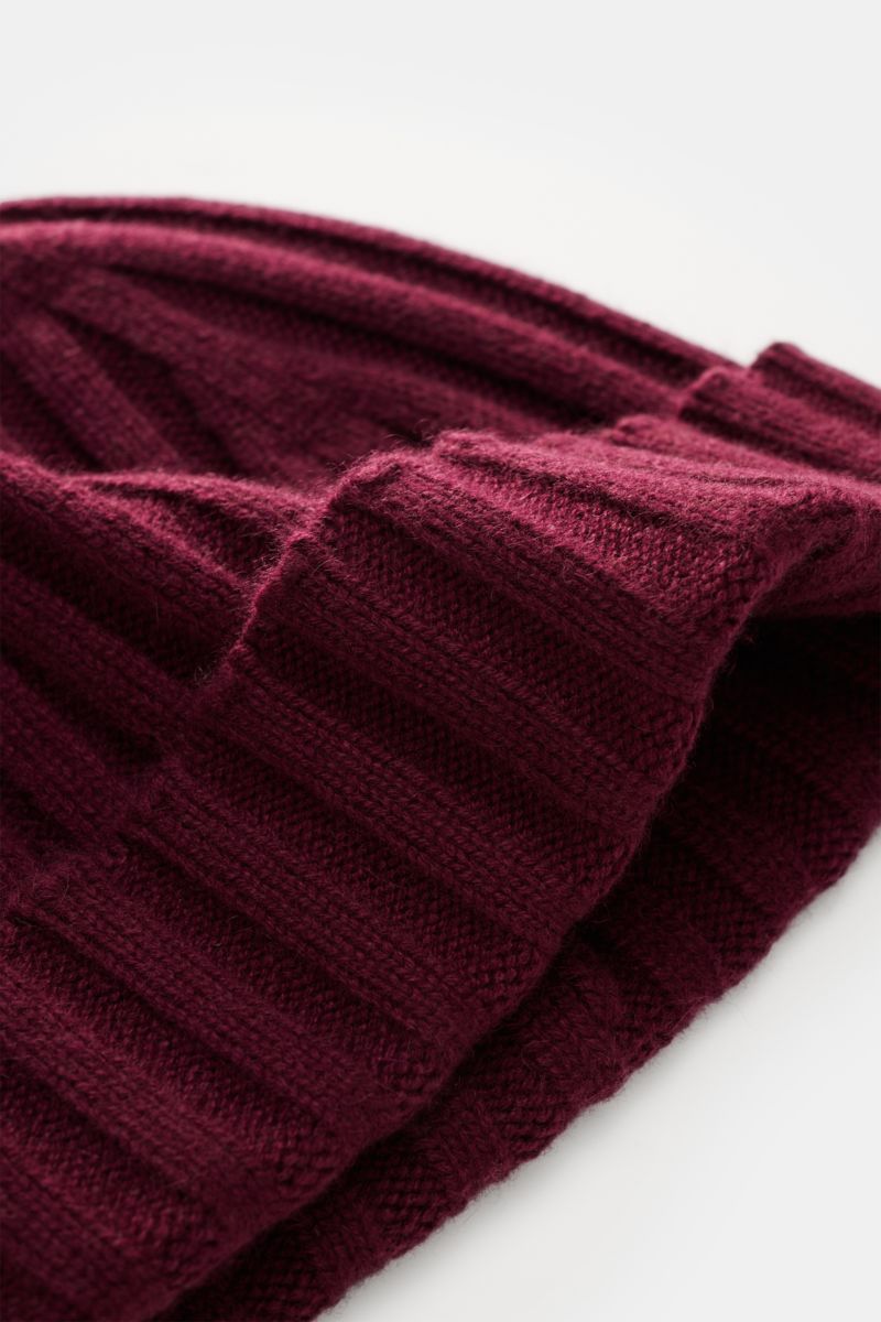 Nahaufnahme der von Braun Cashmere Mütze bordeaux aus reinem mongolischem Cashmere, schmaler Umschlag, feines Rippstrickmuster, sehr weich, aus schräger Perspektive.