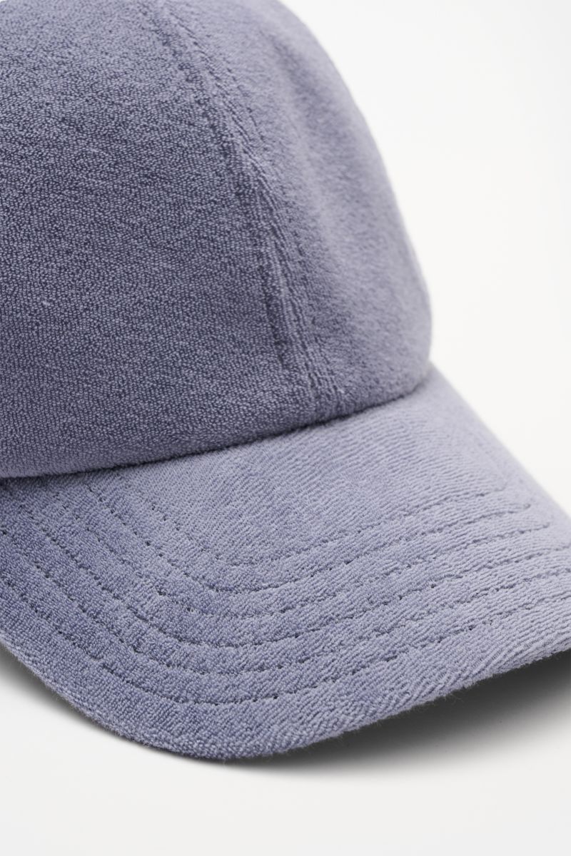 Close-up front-side view of the 04651/ A trip in a bag Terry baseball cap 'Terry' smoky blue in soft cotton terry fabric with six-panel style and adjustable closure, offering a soft feel and sporty yet trendy preppy look. Spring awakening: This stylish ba