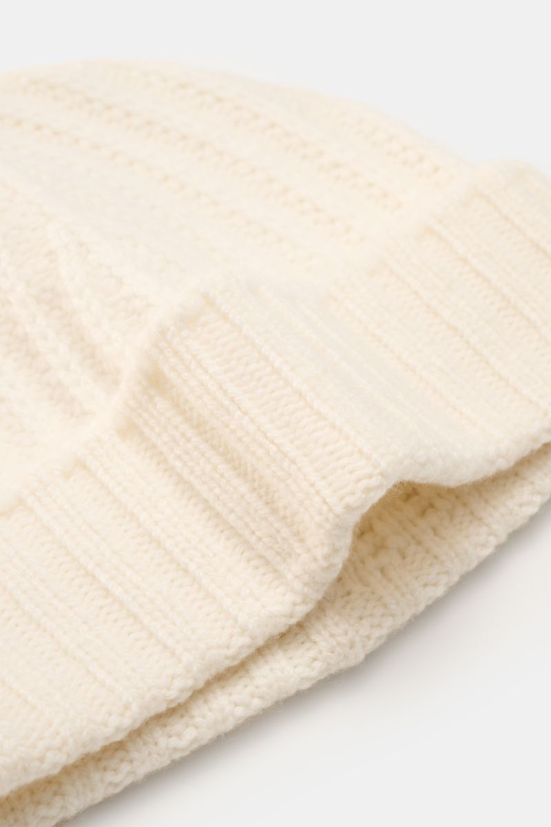 Close-up front-side view of the 04651/ A trip in a bag Cashmere Mütze creme, a luxurious winter accessory in cream with a soft feel, pure cashmere, wide cuff, medium knit pattern, and ribbed stitch.

Description: Luxuriöses Winter-Accessoire
