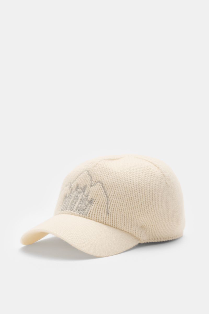 Front-left view of the 04651/ A trip in a bag Cashmere Baseball-Cap creme in pure cashmere with soft feel, medium knit, fine-knit visor, and embroidered Milan Cathedral and Cortina mountain peaks.