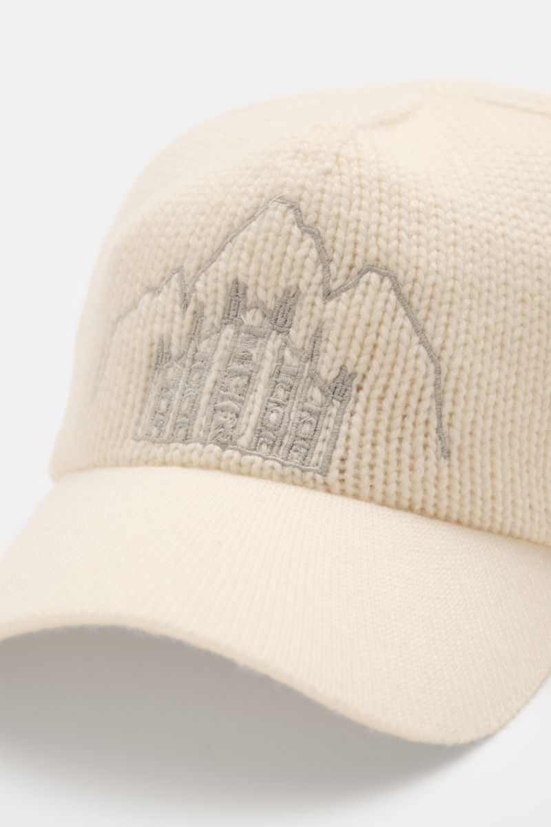 Close-up front-side view of the 04651/ A trip in a bag Cashmere Baseball-Cap creme, featuring pure cashmere with soft touch, medium knit, fine knit brim, and detailed front stitching of Milan Cathedral and Cortina mountain peaks, a luxurious winter highli