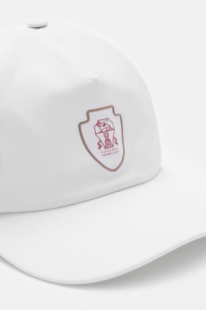 Brunello Cucinelli Baseball-Cap weiß shown from a front-side angle with Solomeo logo patch, perforations, smooth microfiber, wide brim, and adjustable closure. Inspiriert vom Tennissport: Diese Cap aus dem Hause BRUNELLO CUCINELLI setzt mit dem Solomeo-Lo