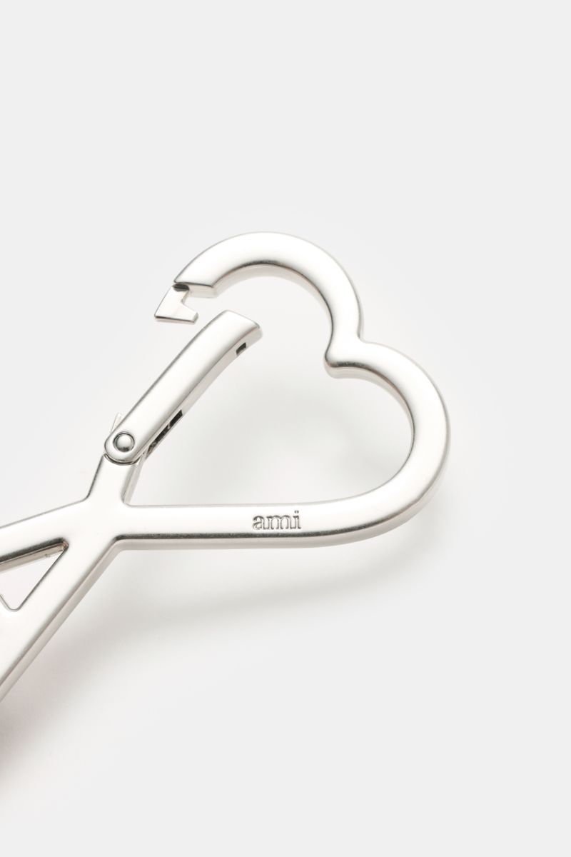 Ami Paris Schlüsselanhänger silber shown from a close-up top angle, featuring a heart-shaped AMI-logo carabiner with 'ami' engraving, approx. 8 x 5 cm. Unisex Accessoire von AMI PARIS: Dieser praktische Begleiter mit dem markentypischen 'A' mit Herz hä