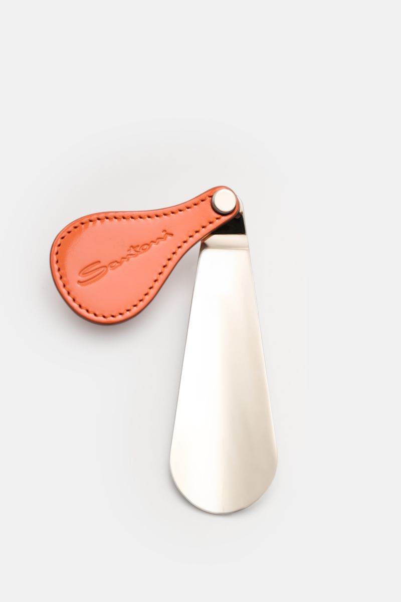 Top view of the Santoni Schuhlöffel silber shoehorn with a metal spoon and flexible orange leather handle embossed with SANTONI.

Der praktische Schuhlöffel mit Ledergriff von SANTONI erfüllt mit seiner handlichen Größe auch auf Reisen seinen Zweck.