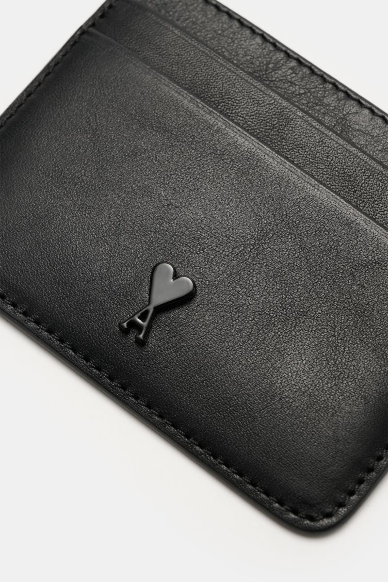 Close-up, angled view of the Ami Paris Kartenetui schwarz made of finely grained black calf leather, featuring a front logo, one central compartment, and four card slots, measuring approximately 10 cm x 8 cm. Stilvolles Accessoire für den Alltag: Diese