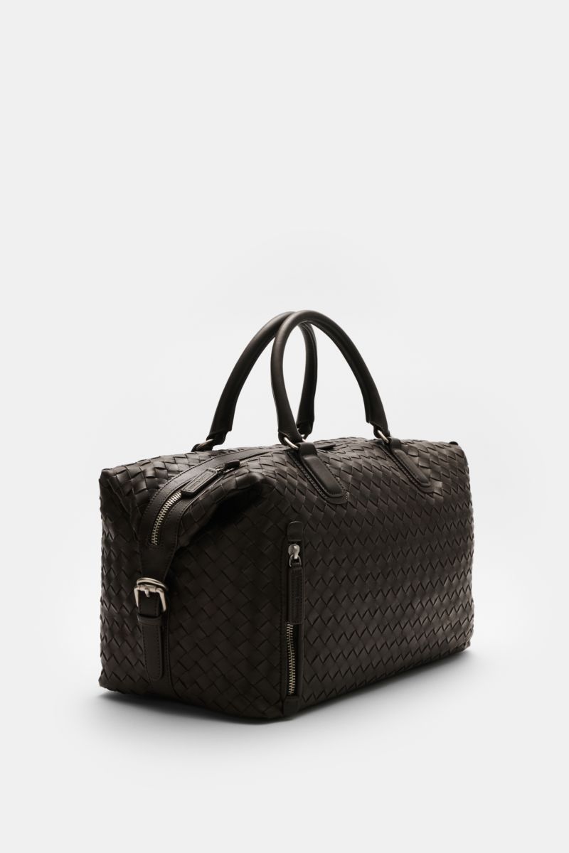 Side perspective of Officine Creative Weekender dunkelbraun, a spacious, variably portable weekender made of handwoven, finely grained dark brown leather with matte silver hardware, robust handles, adjustable/removable shoulder strap, two-way zipper, fron